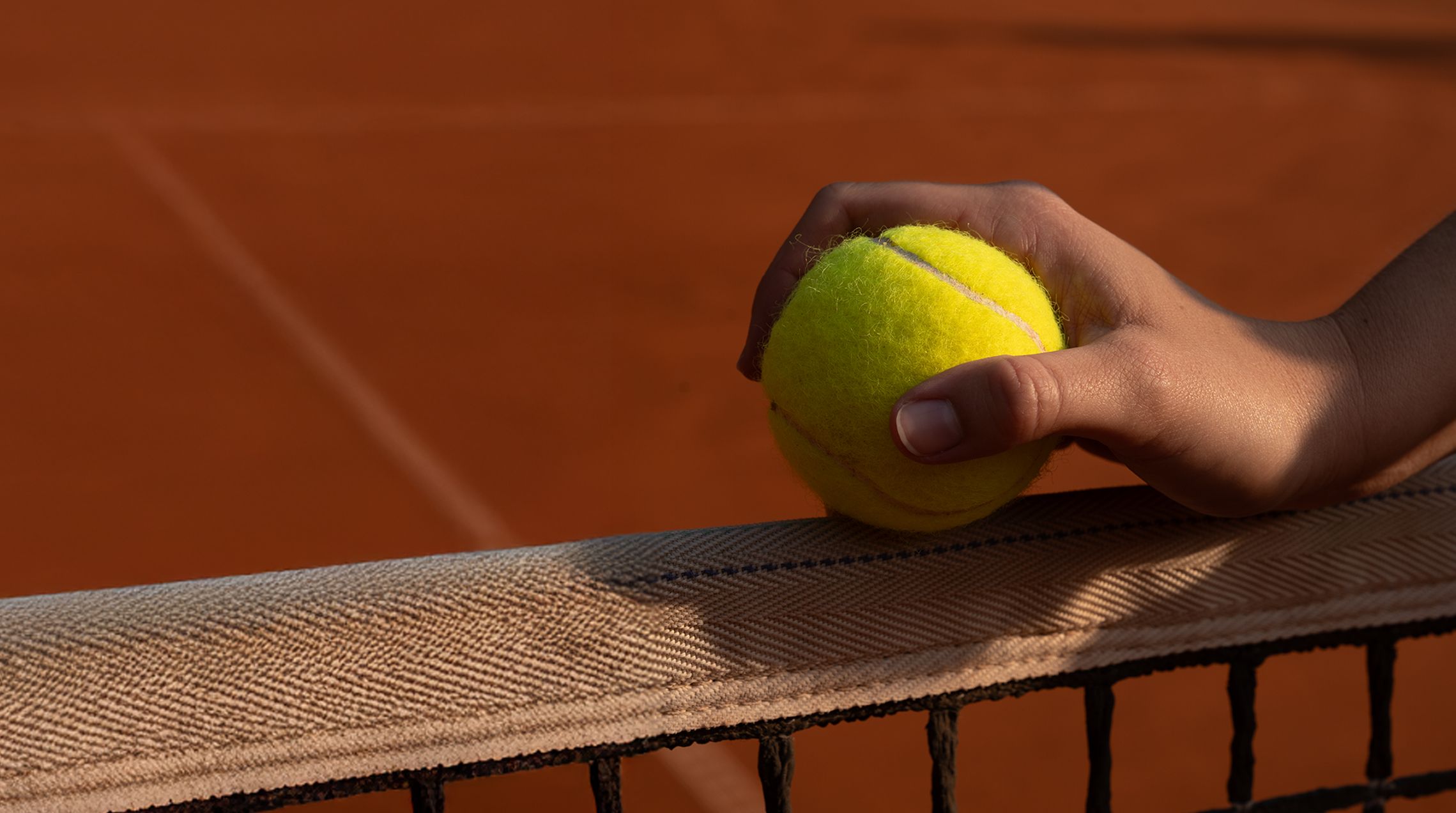 Nahaufnahme einer Hand, die einen Tennisball auf einem Netz abstützt