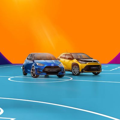 Drei moderne SUVs in Schwarz, Rot und Gelb stehen auf einem pinkfarbenen Basketballfeld vor einer abstrakten Kulisse mit großen orangefarbenen und blauen geometrischen Formen.