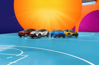 Vier Toyota-Fahrzeuge in Rot, Blau, Gelb-Schwarz und Grau vor einem farbigen, grafischen Hintergrund, nebeneinander auf einer stilisierten Fläche präsentiert.