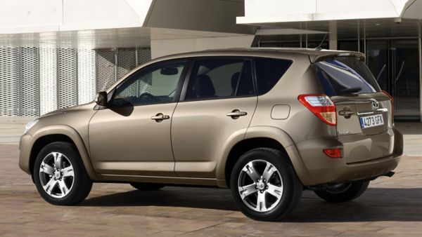 Brązowa Toyota RAV4 zaparkowana przed nowoczesnym budynkiem z metalową fasadą