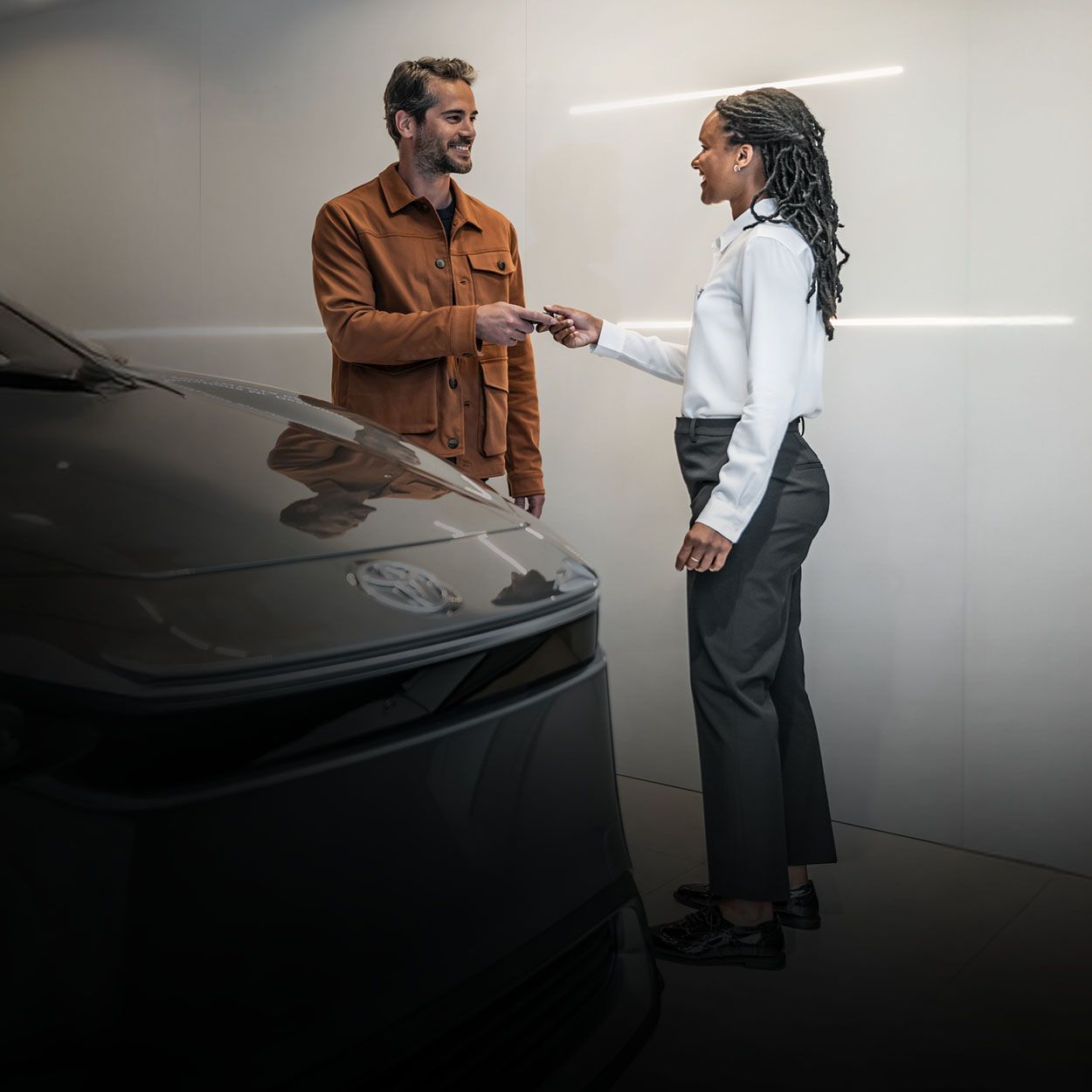 Eine Autohaus-Mitarbeiterin übergibt einen Schlüssel an einen Kunden. Beide stehen vor einem Toyota bZ4X
