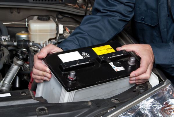 Ein Mechaniker setzt eine schwarz-weiße Batterie in den offenen Motorraum eines Autos ein.