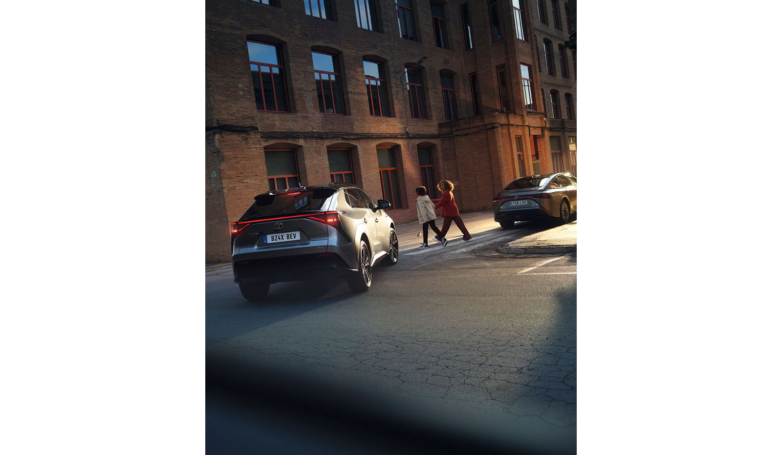 Blick von hinten auf einen Toyota bZ4X, der beim Abbiegen in der Stadt bremst, um zwei Personen an einem Zebrastreifen passieren zu lassen