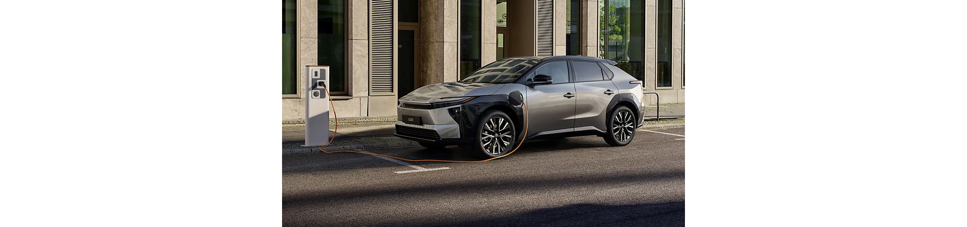 Toyota bZ4X – elektryczny SUV zaparkowany na miejskiej ulicy obok punktu ładowania pojazdów elektrycznych.