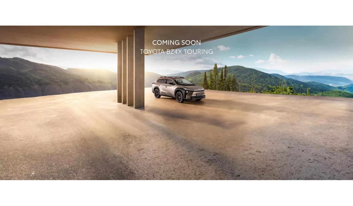 Lichtgrijze Toyota bZ4X Touring SUV geparkeerd onder een moderne betonnen structuur, met uitzicht op een berglandschap badend in zonlicht. Tekst bovenaan de afbeelding “COMING SOON - TOYOTA BZ4X TOURING”.