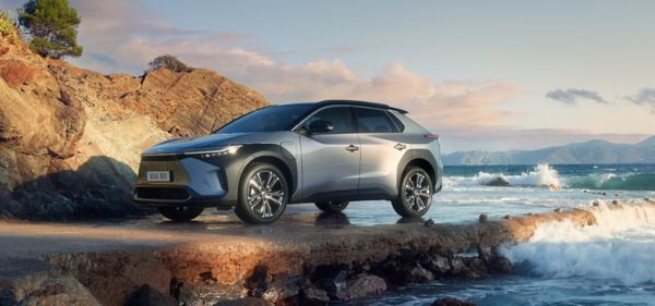 Silberner Toyota SUV parkt an felsigem Strand, dahinter brechen sich Wellen.