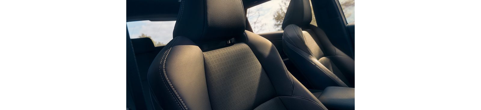 Blick durch das geöffnete Fenster auf die Vordersitze des Toyota bZ4X, die von der Sonne bestrahlt werden, während im Hintergrund vereinzelt Bäume zu sehen sind.