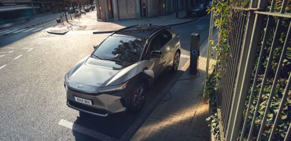 Ein silberner Toyota bZ4X steht geparkt am Straßenrand und lädt an einer Ladesäule.