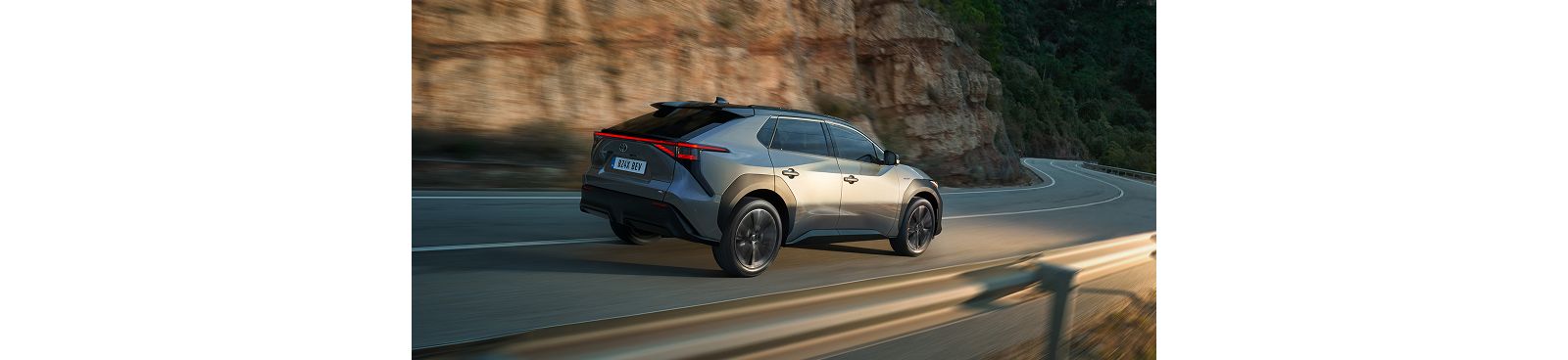 Ein silbergrauer Toyota bZ4X fährt im Abendlicht auf einer Straße vor einer Felswand
