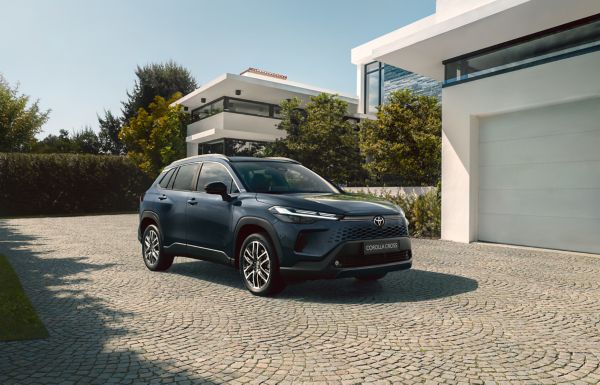 Blaues SUV steht auf einer gepflasterten Hauseinfahrt vor einer Garage und wird von der Sonne angestrahlt.