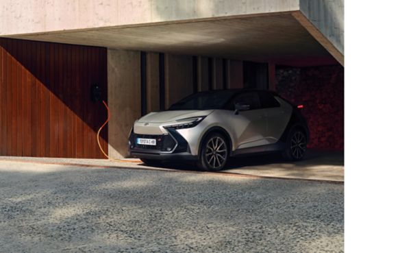 Woman sitting by the window of a modern home, above a Toyota CH-R charging with the Toyta HomeCharge 