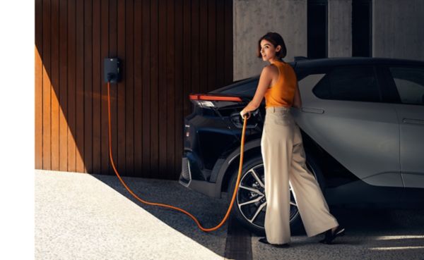 Woman plugging in her Toyota CH-R to charge with the Toyota Homecharge with modern house in the background 