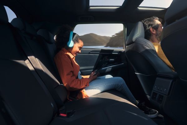 Kind mit blauen Kopfhörern sitzt auf dem Rücksitz eines Autos und schaut auf ein Tablet auf dem Schoß.