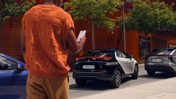 Egy Toyota C-HR felé sétáló személy telefonjával