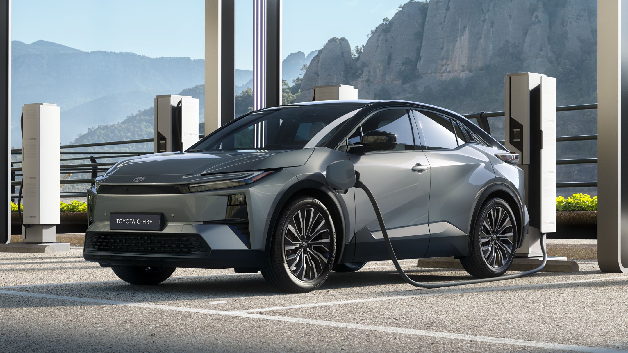 Grauer Crossover-SUV von Toyota steht in einem Parkhaus und lädt an einer Ladesäule. Im Hintergrund ist eine bergige Landschaft zu sehen.