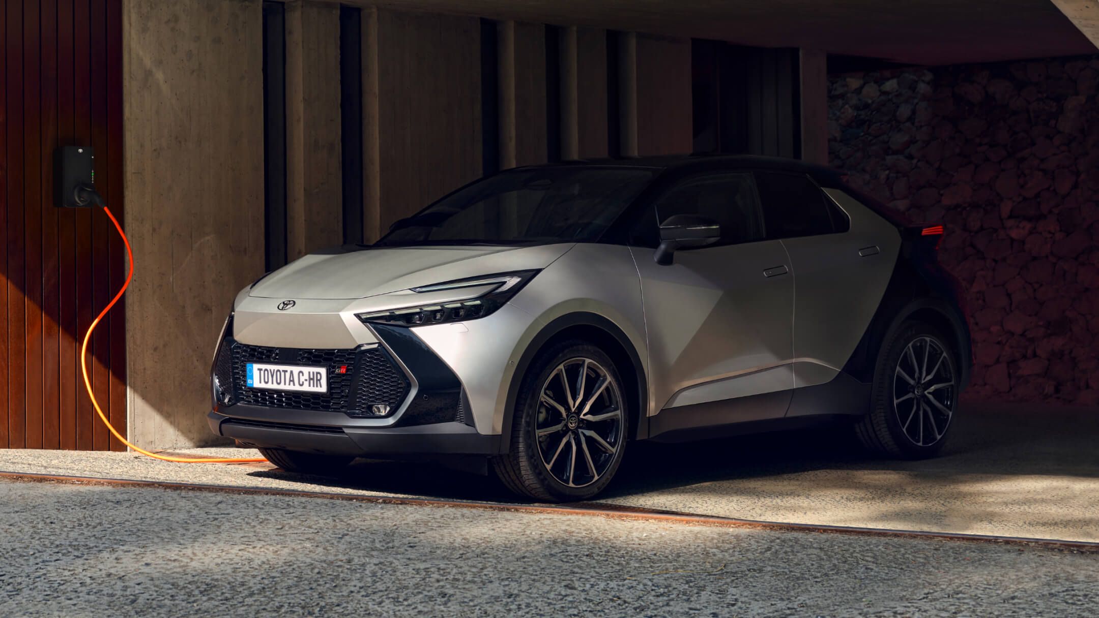 Silbernes Kompakt-SUV von Toyota steht überdacht in einer modernen Hauseinfahrt und lädt an einer Wallbox.