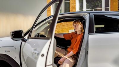 Eine Person sitzt auf dem Fahrersitz eines weißen Autos mit geöffneter Fahrertür.