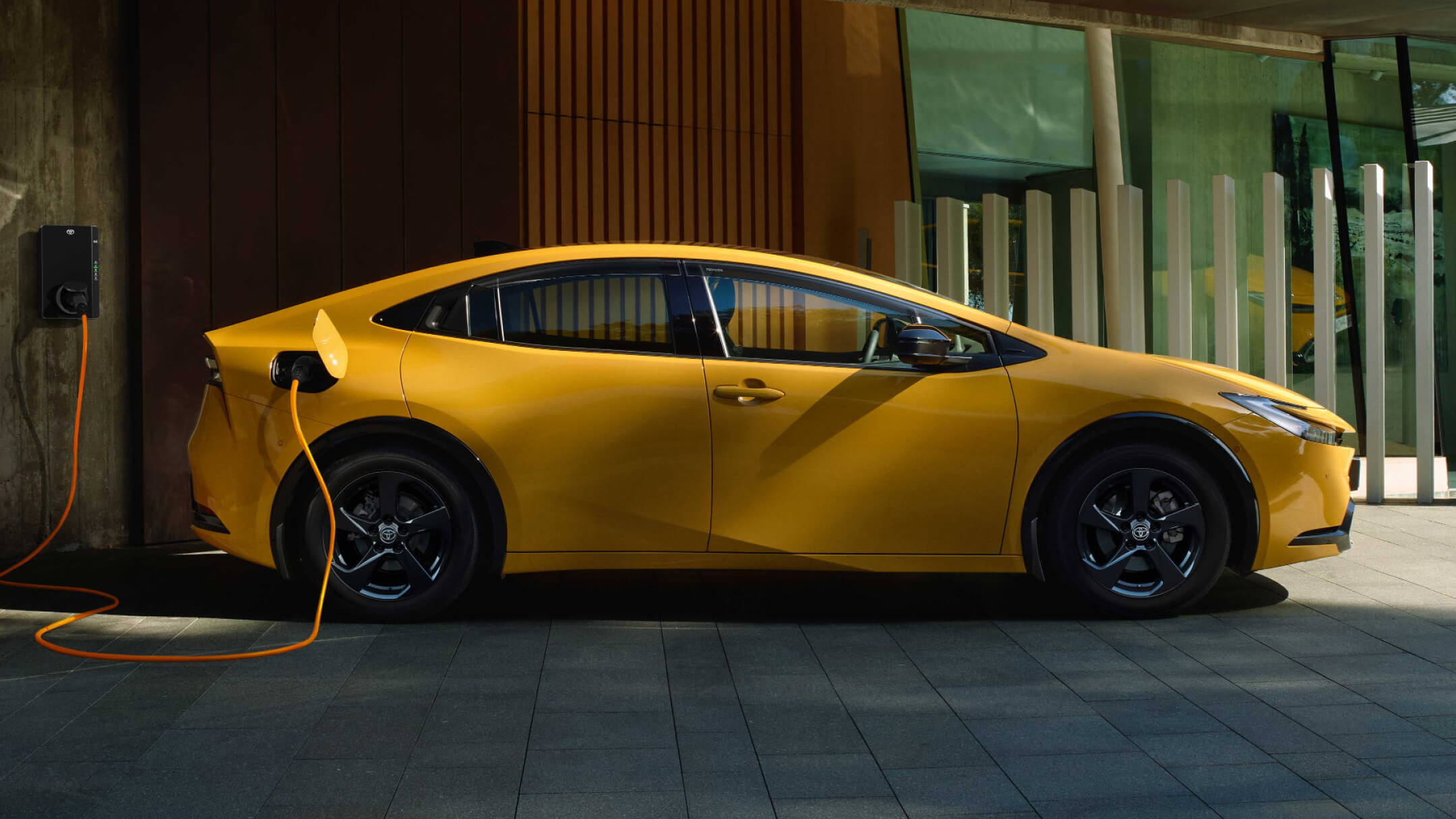 Gelber Plug-in Hybrid von Toyota steht unter einem Carport und lädt an einer Wallbox.