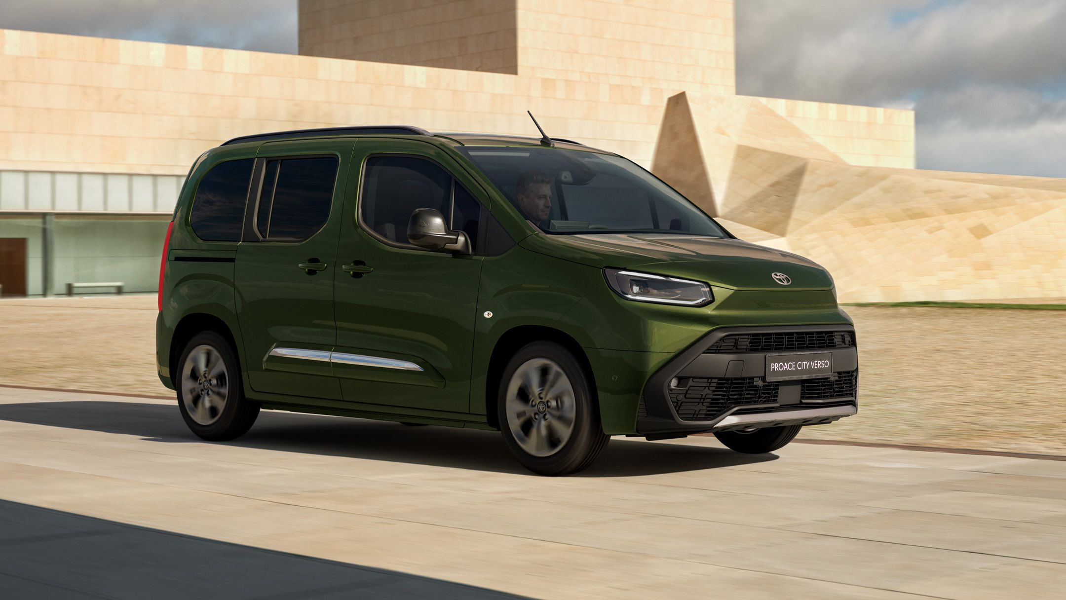 Grüner Elektro-Van fährt vor einem sandsteinfarbenen Gebäude entlang.