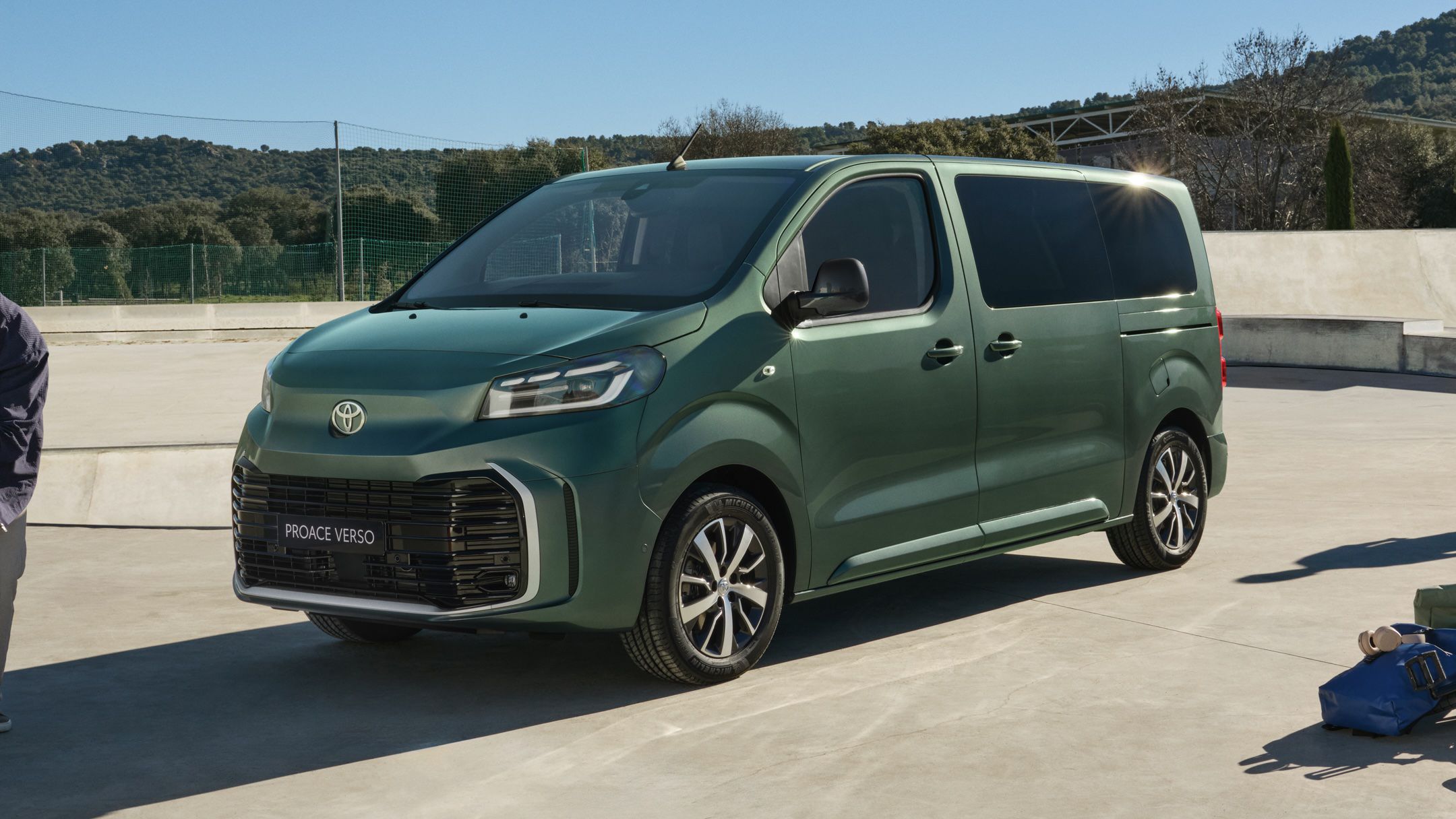 Grüner Elektro-Van steht geparkt auf einem betonierten Skatepark. Im Hintergrund ist ein grüner Stück Wald zu sehen.