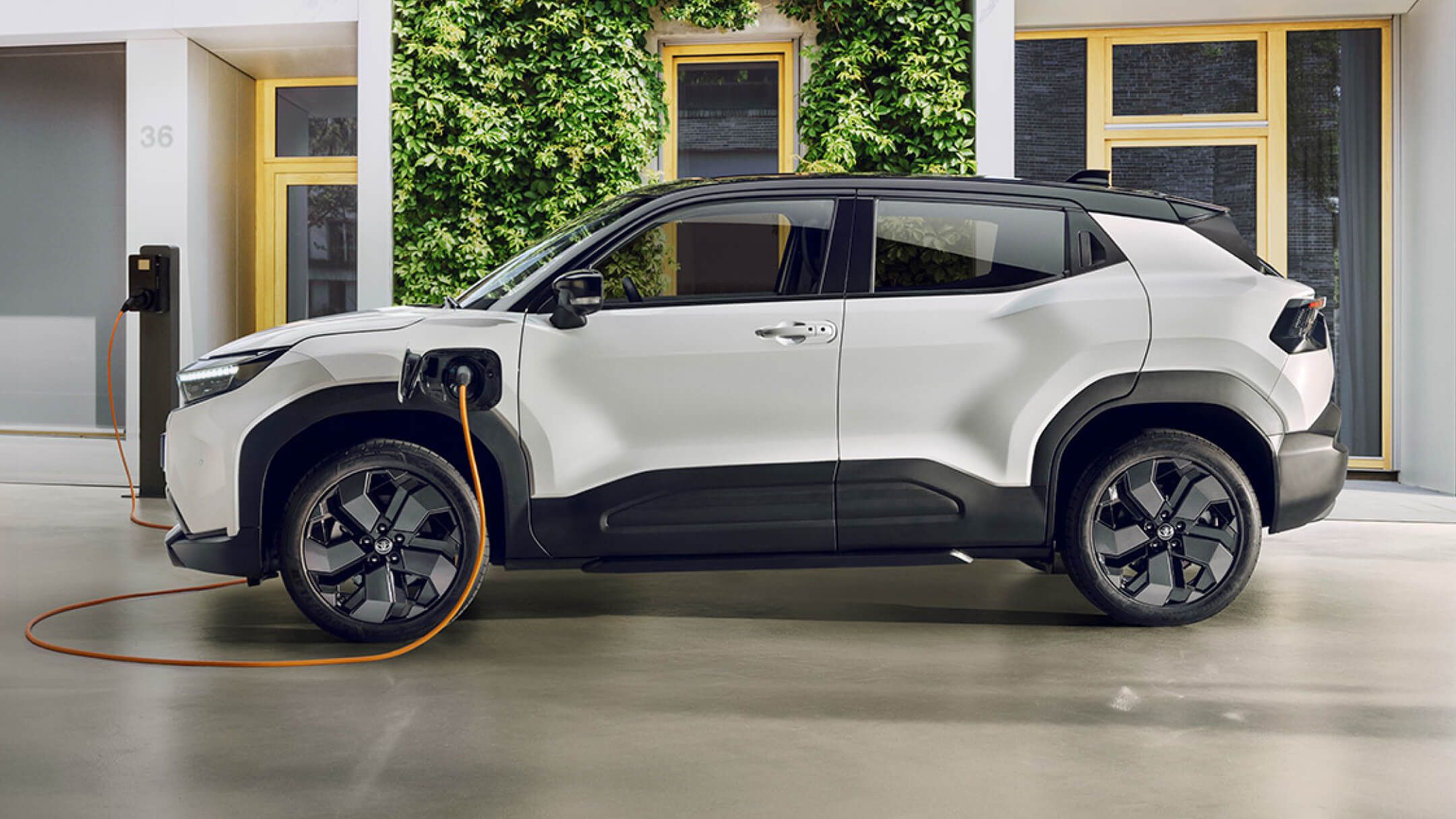 Schwarzer Urbanes Crossover-SUV steht seitlich zur Kamera und lädt an einer Ladesäule. Dahinter ist eine grüne Fassade eines Gebäudes zu sehen.