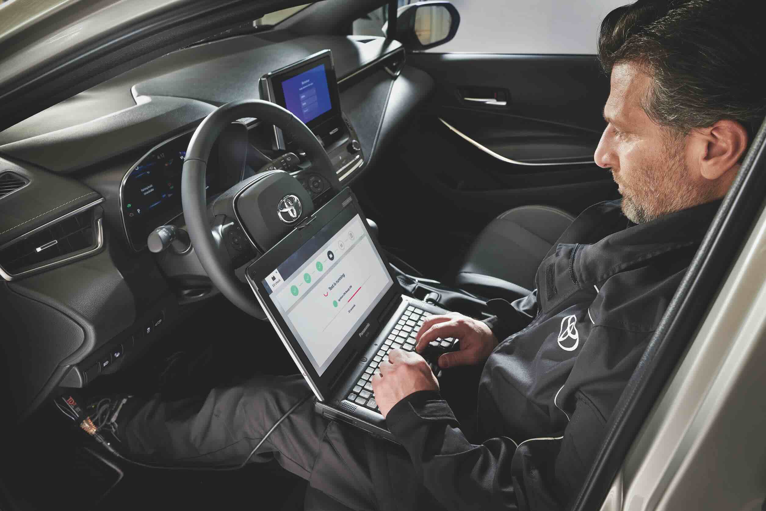 Person kontrolliert im Innenraum eines Fahrzeugs an einem Laptop die Fahrzeugdaten