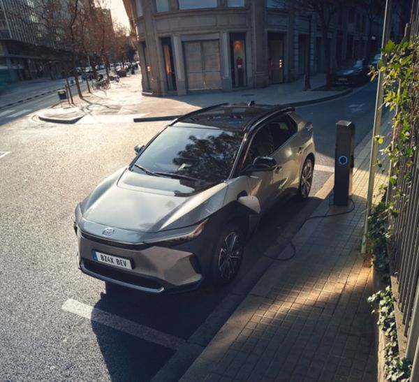 Ein silberner Toyota bZ4X steht geparkt am Straßenrand und lädt an einer Ladesäule.