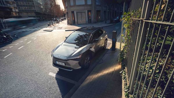 Ein silberner Toyota bZ4X steht geparkt am Straßenrand und lädt an einer Ladesäule.