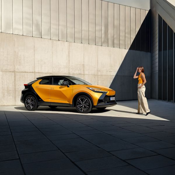Ein schwarz-orangener Toyota C-HR steht in einem Innenhof. Eine Person läuft darauf zu.
