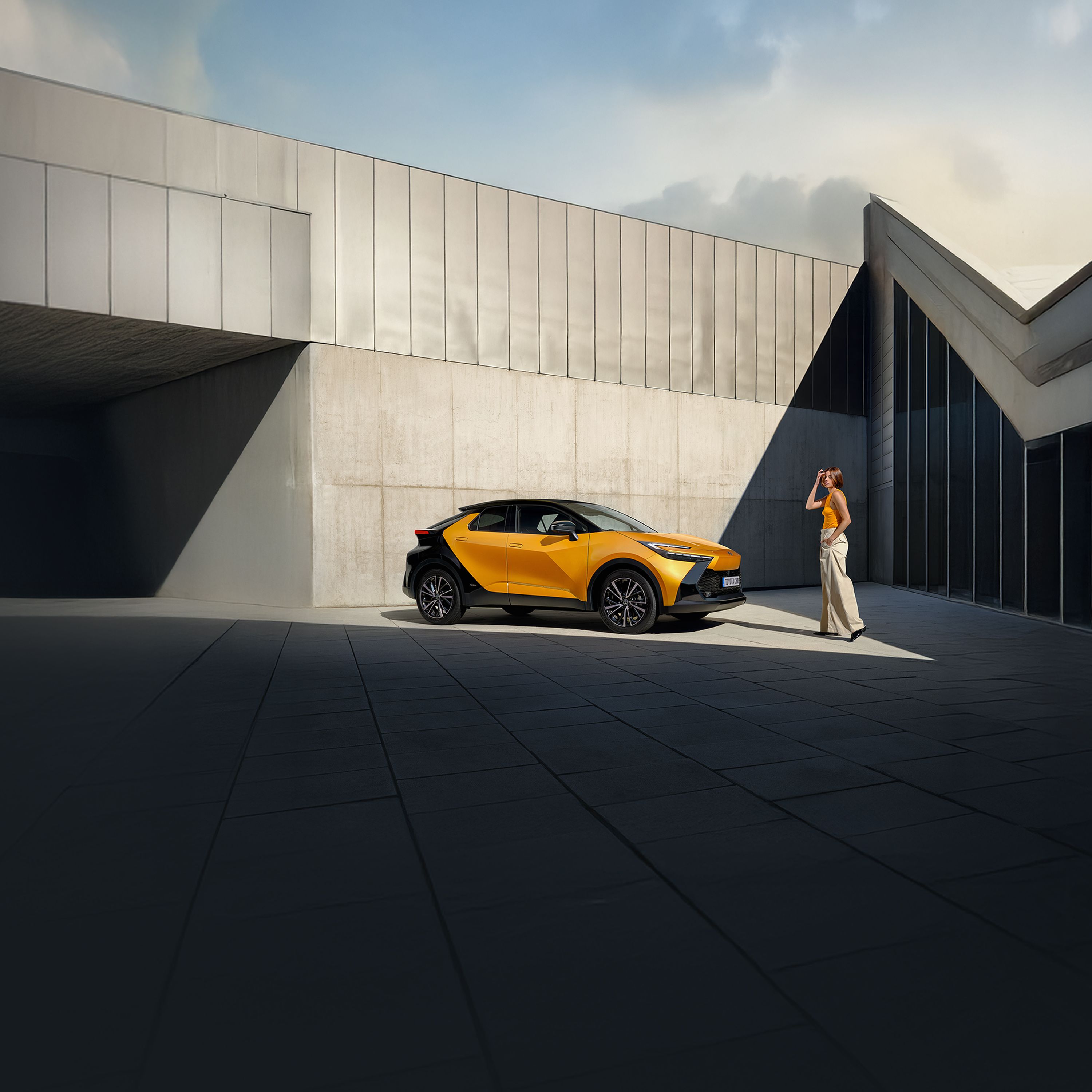Eine Person in orangenem Outfit geht auf einen orange-schwarzen Toytoa C-HR zu.