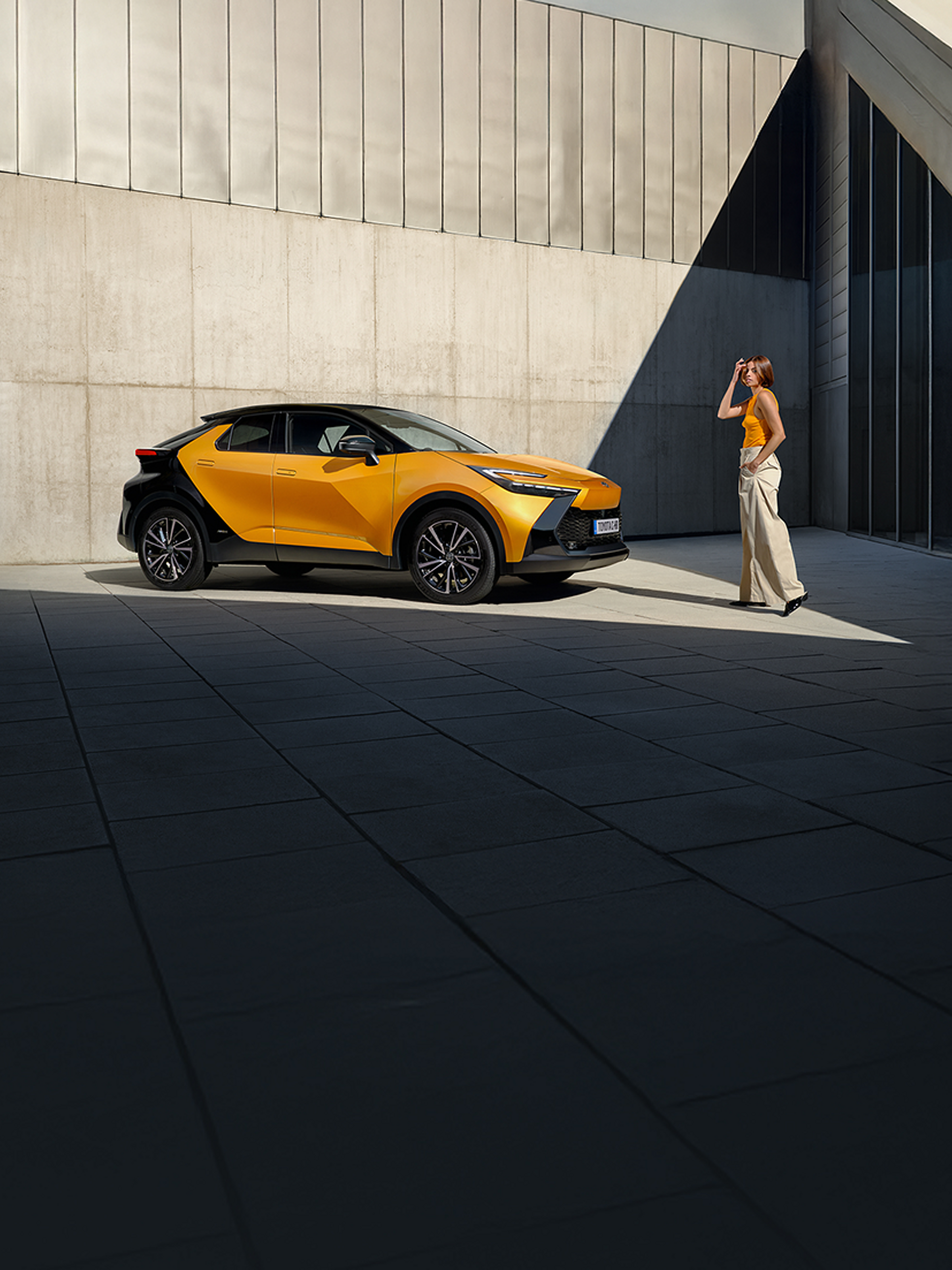 Ein schwarz-orangener Toyota C-HR steht in einem Innenhof. Eine Person läuft darauf zu.