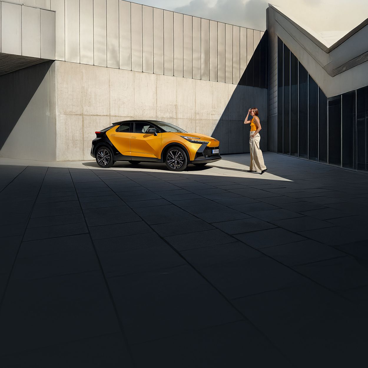 Eine Person in orangenem Outfit geht auf einen orange-schwarzen Toytoa C-HR zu.
