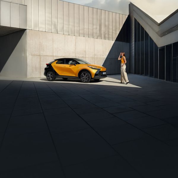 Ein schwarz-orangener Toyota C-HR steht in einem Innenhof. Eine Person läuft darauf zu.