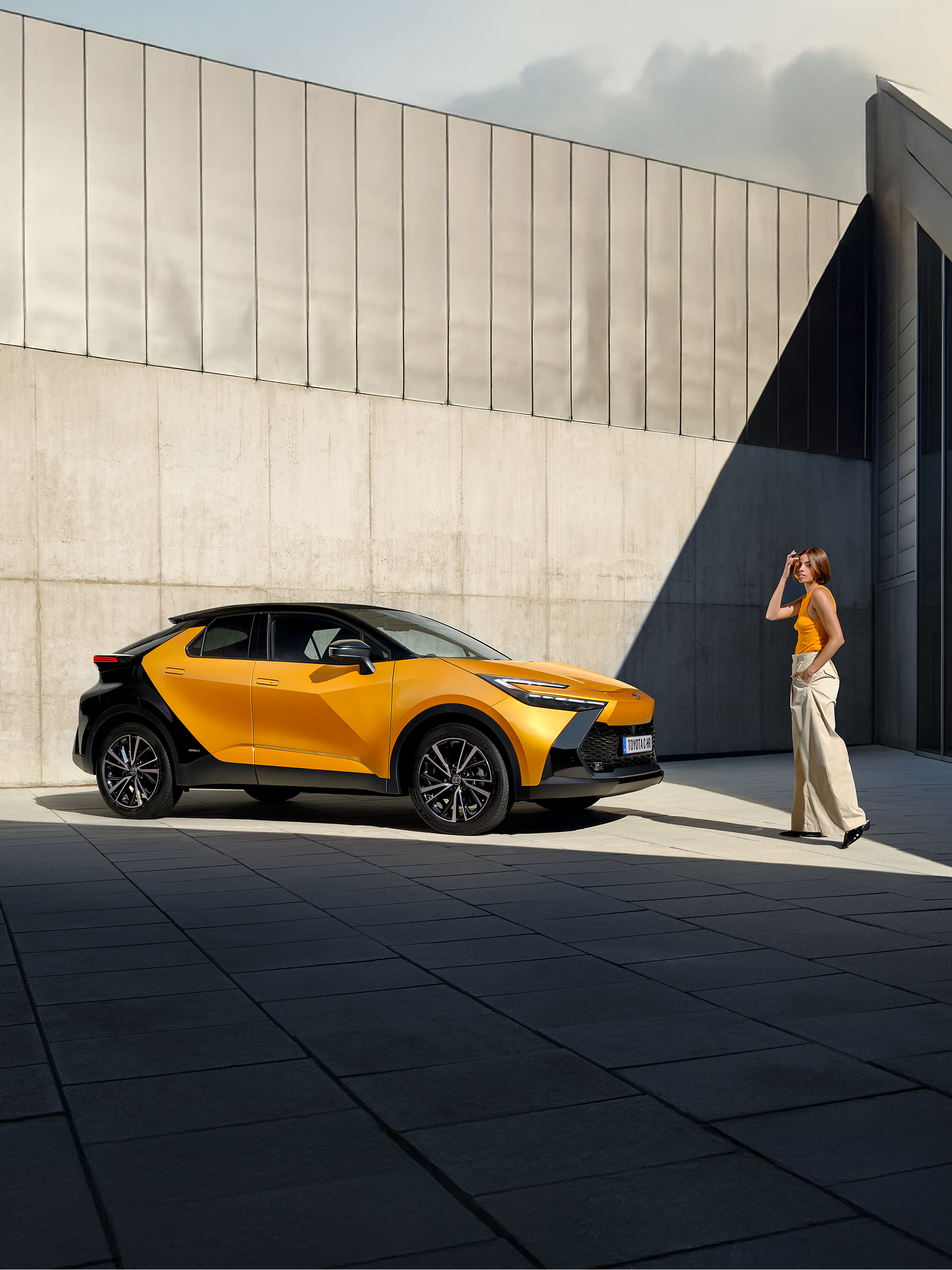 Ein schwarz-orangener Toyota C-HR steht in einem Innenhof. Eine Person läuft darauf zu.