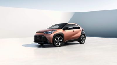 Bronzefarbener Aygo X steht diagonal zur Kamera vor einem neutralem Hintergrund.