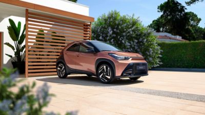 Bronzener Aygo X steht geparkt vor einem Haus.