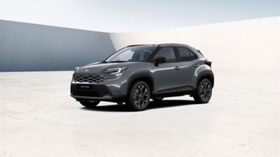 Grauer Toyota Yaris Cross steht diagonal zur Kamera vor einem neutralem Hintergrund.