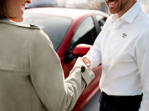 Zwei Personen stehen vor einem roten Wagen und schütteln sich die Hände. Die eine Person trägt ein Hemd mit aufgedrucktem Toyota Logo