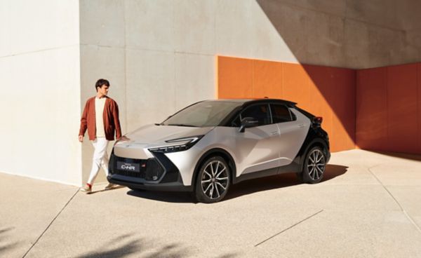 Person läuft an einem geparkten Toyota C-HR entlang, der vor einer weiß-terracotta Wand steht.