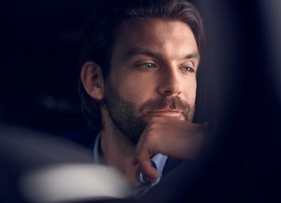 Ein Geschäftsmann sitzt nachdenklich im Firmenwagen und blickt aus dem Fenster, während er seine nächste Fahrt mit dem Dienstauto plant.