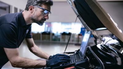 Ein Service-Mitarbeiter schaut auf ein Laptop, das aufgeklappt im Motorraum eines Fahrzeugs steht.