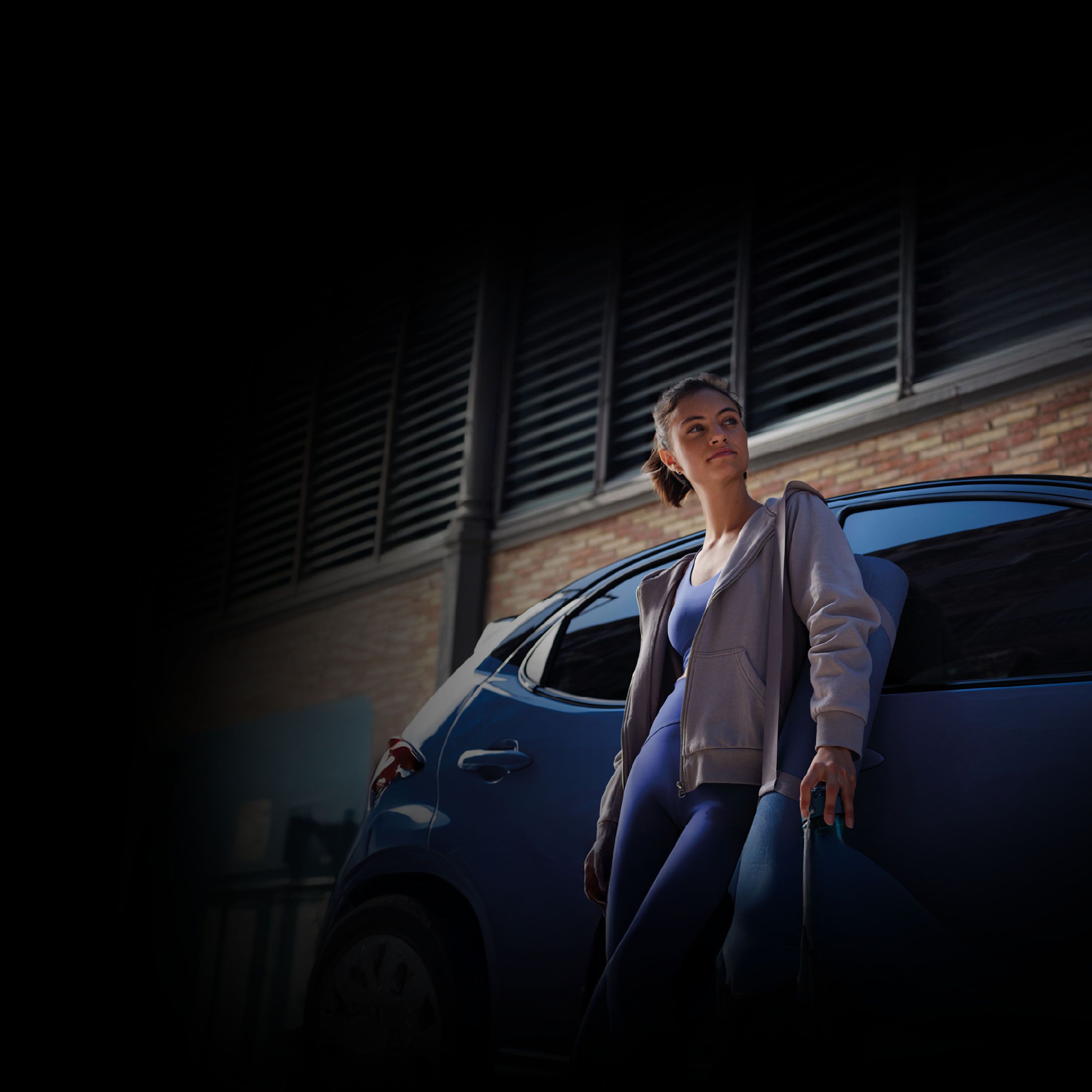 Eine Frau in grüner Jacke und mit dunkler Sonnenbrille sitzt am Steuer eines Toyota.