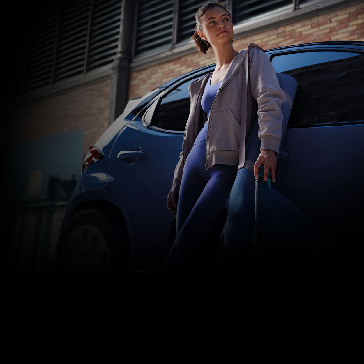 Eine Frau in einem sportlichen Outfit lehnt lässig an einem Toyota