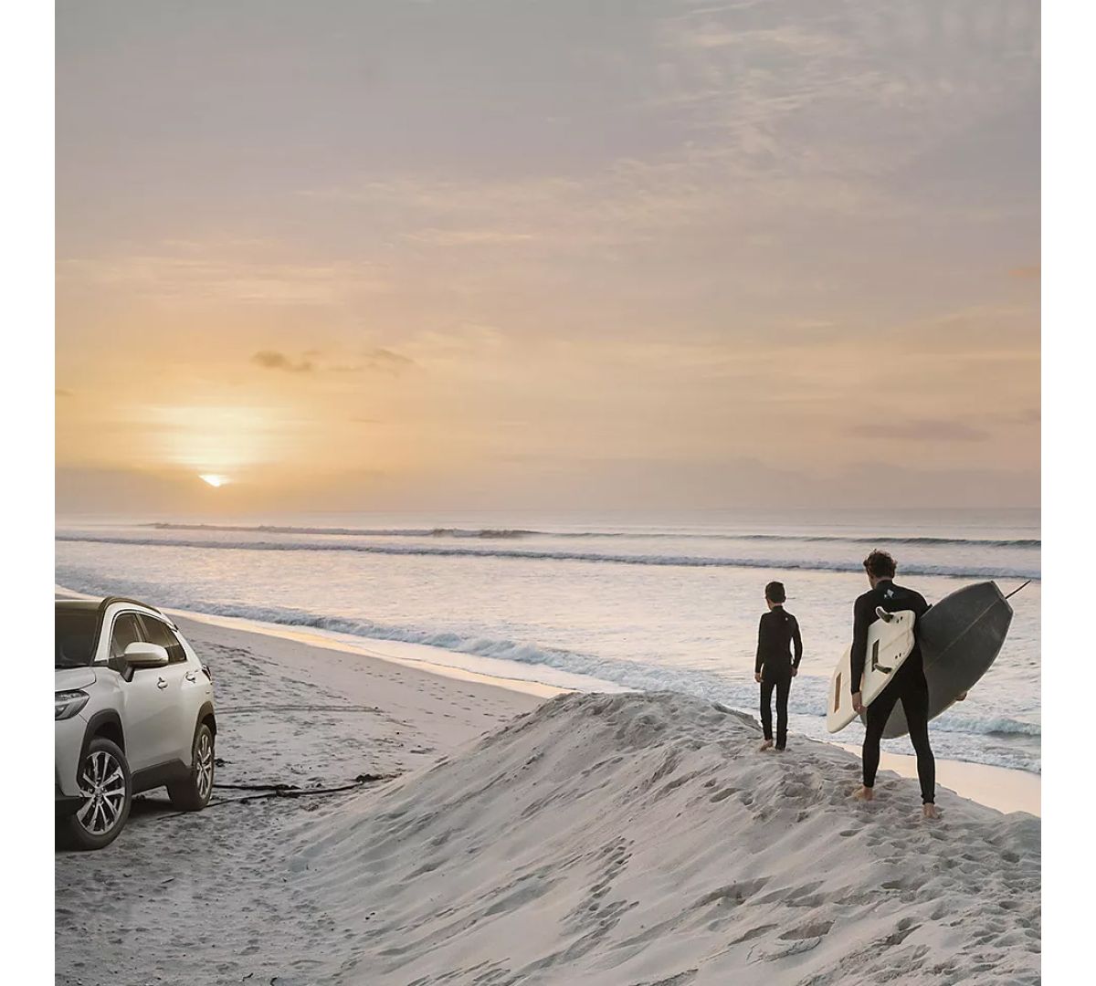 Ein Mann und ein Kind laufen auf einer Sanddüne am Meer entlang, neben ihnen steht ein geparkter Toyota