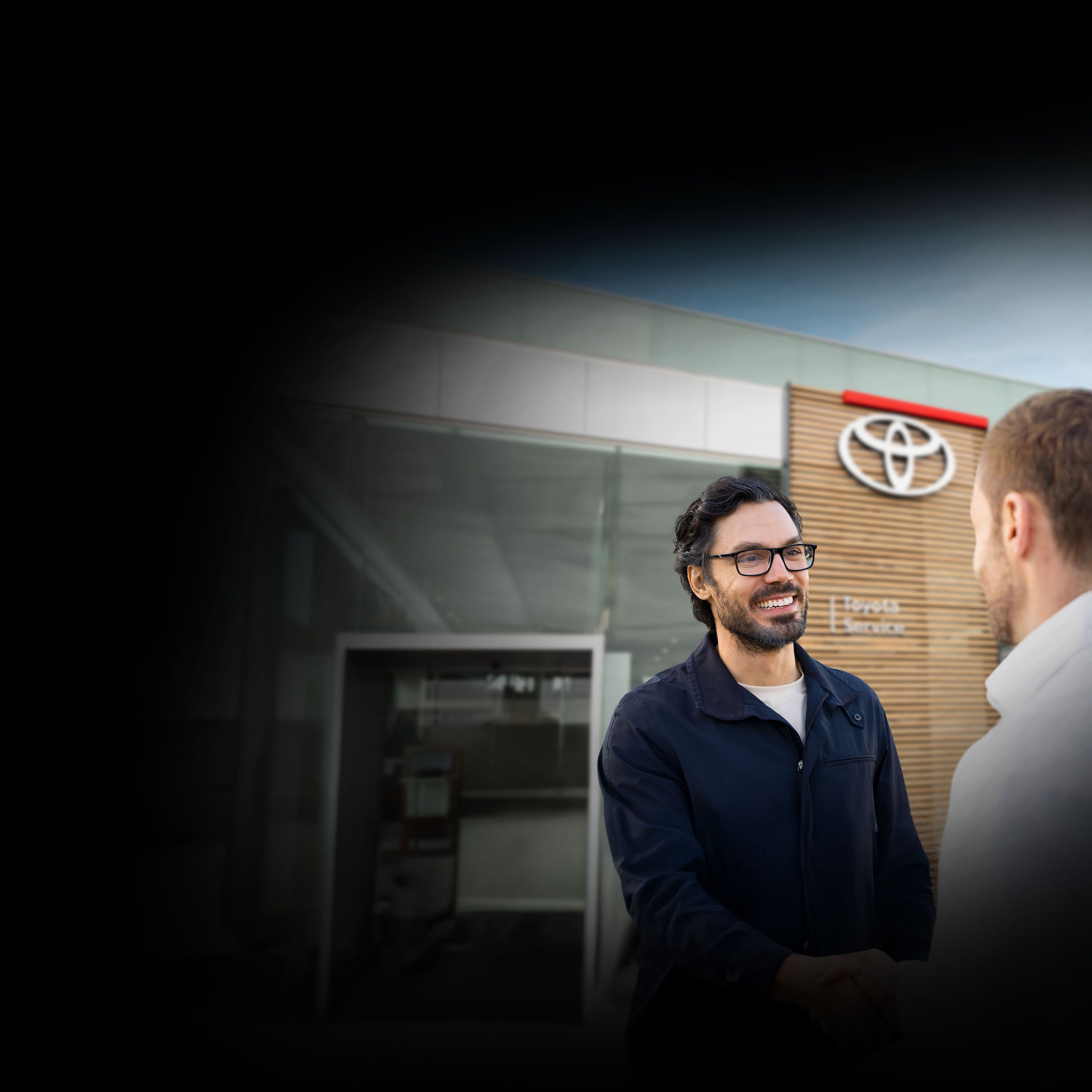 Zwei Männer stehen vor einem Toyota Autohaus und unterhalten sich