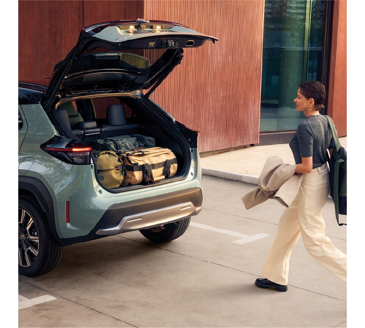Eine Frau geht auf einen Toyota mit geöffneter Kofferraumklappe zu in der sich mehrere Taschen befinden