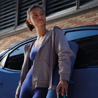 Eine Frau in einem sportlichen Outfit lehnt lässig an einem Toyota