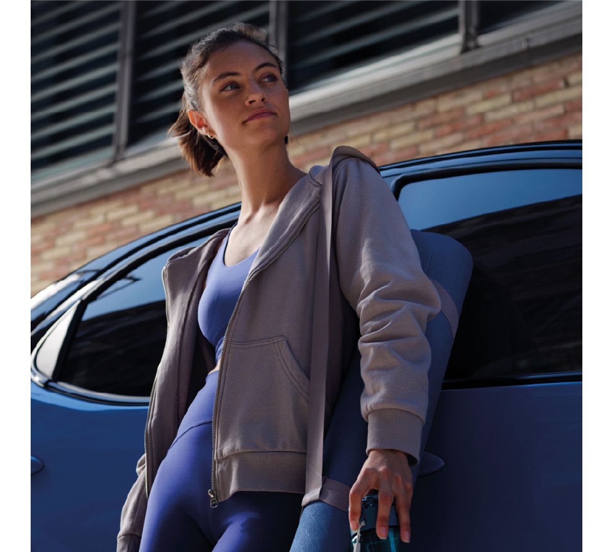 Eine Frau in einem sportlichen Outfit lehnt lässig an einem Toyota