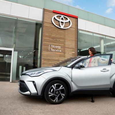 Eine Frau steigt in einen Toyota, der vor einem Toyota Auttohaus geparkt steht.