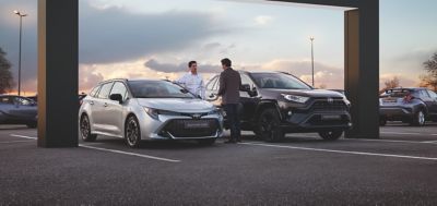 Zwei Personen unterhalten sich zwischen einem Corolla TS und Toyota RAV4.